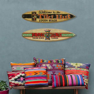 Welcome to the Tiki Hut - Surfboard Wall Art displayed above colorful patterned pillows on a blue wall background
