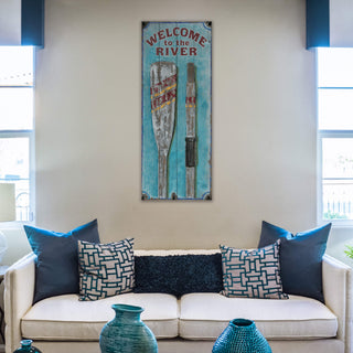 Lake Welcome with Oars - Wood & Metal Wall Art hanging above couch with blue and patterned pillows in modern living room